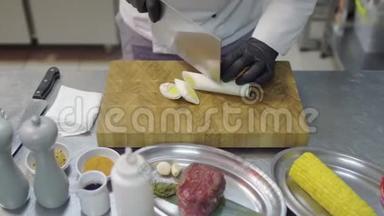 厨师手戴黑色乳胶手套，在砧板上切柠檬草片。 带有厨房用具的厨房餐桌